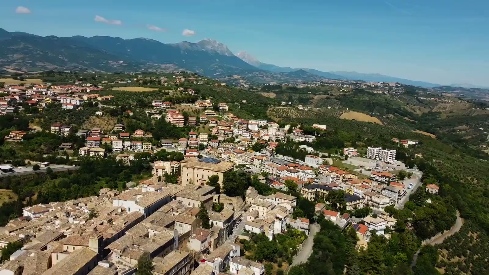 Veduta aerea di Loreto Aprutino sulle colline, con il crinale del Gran Sasso sullo sfondo e gli uliveti sui pendii.